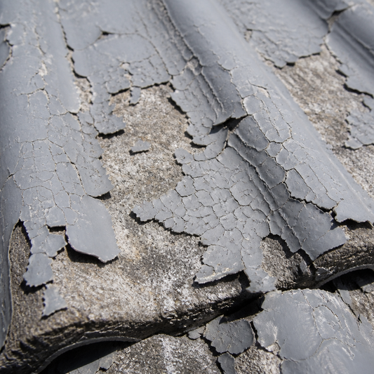Close-up of cracked, peeling grey paint lifting off a weathered concrete roof tile