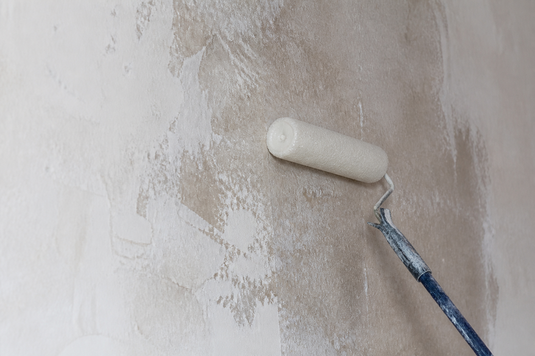 Roller applying clear bonding liquid primer to a chalky interior wall