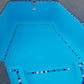 A bright blue swimming pool with blue and white mosaic tile borders, shown from an elevated angle.