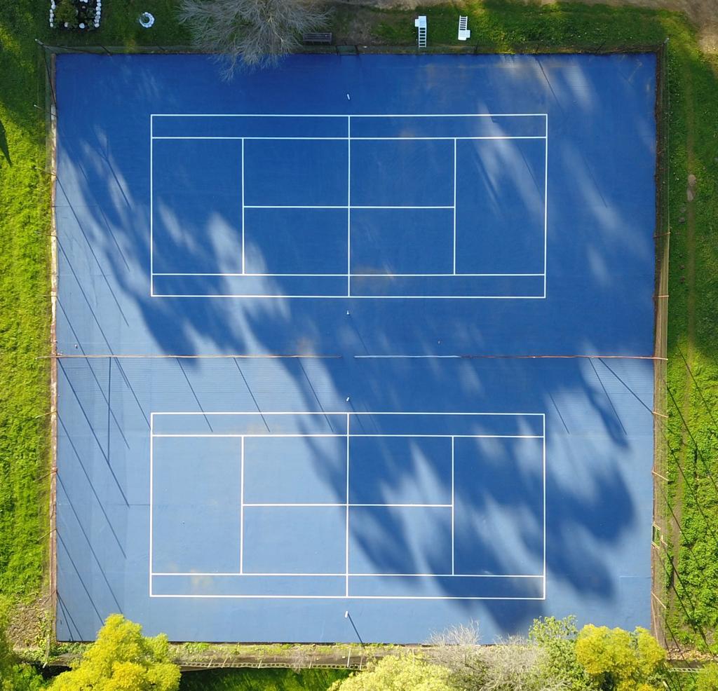Two Blue Tennis Courts surrounded by green grass