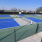 Outdoor pickleball court with blue and green surface, surrounded by a fence.