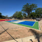 Outdoor sports court with a blue and green surface, surrounded by trees and parked cars.