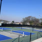 Outdoor pickleball court with blue and gray surface, surrounded by trees and clear sky.