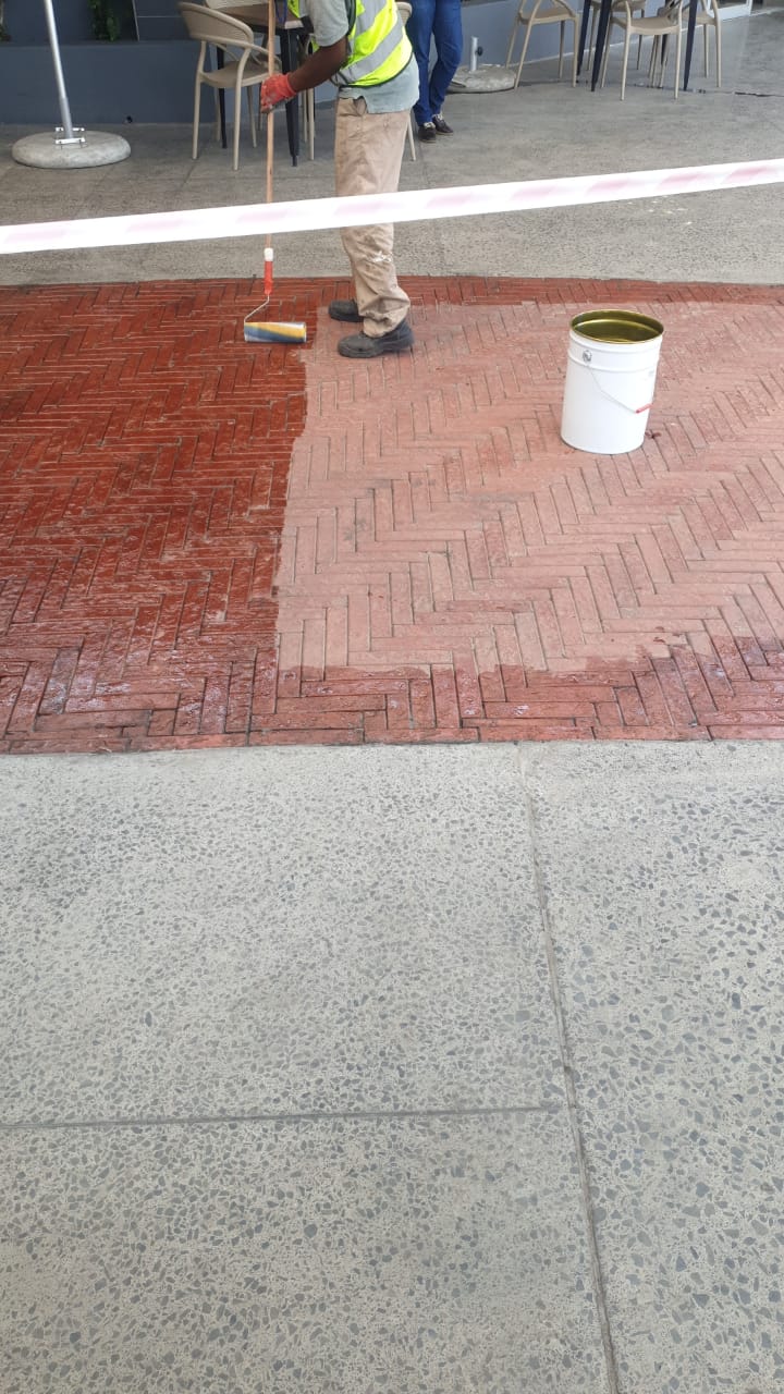 Applying Rhinoluxe Stone Sealer with roller to red clay paver walkway at shopping mall entrance