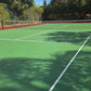 Tennis court with green surface and red border, surrounded by trees.
