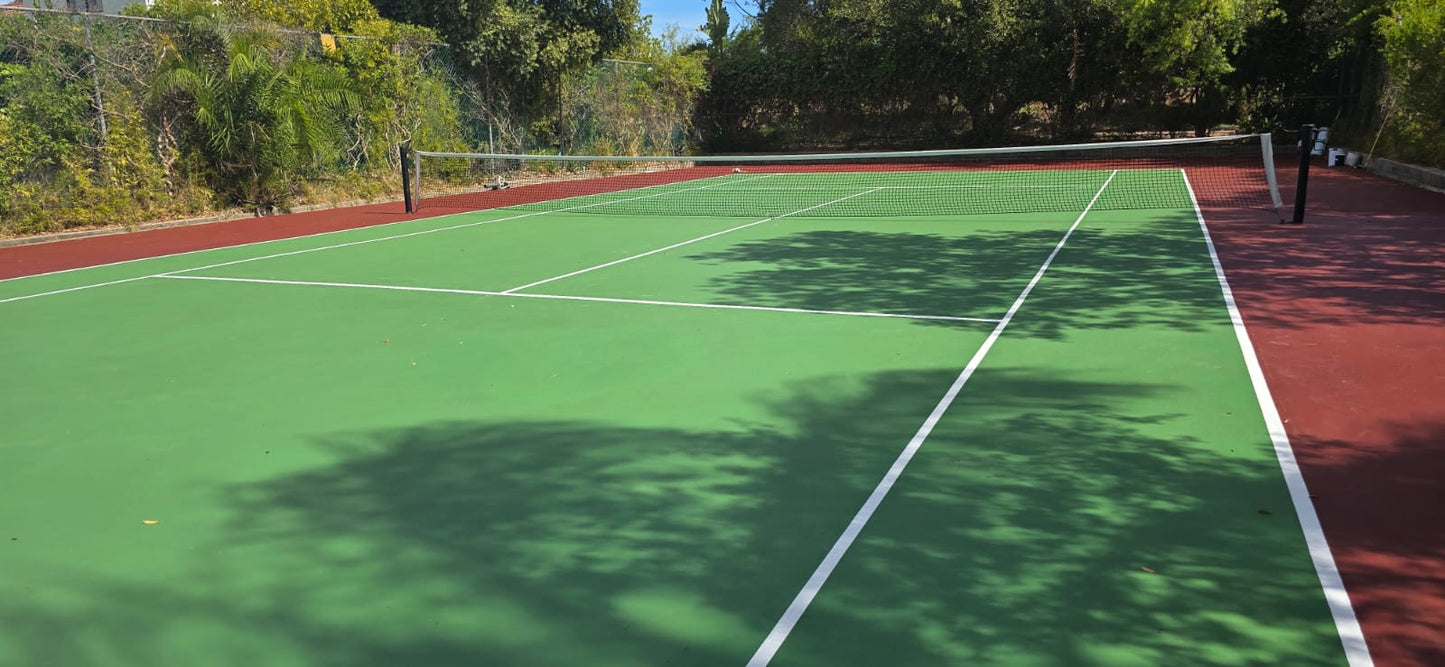 Tennis court with green surface and red border, surrounded by trees.