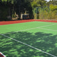 Tennis court with red surface and green playing area, surrounded by trees.